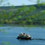 LOOKING THROUGH TREES DOWN TO THE BAY AT DRUMNADROCHIT WHERE THE PLEASURE CRUISER, "THE JACOBITE QUEEN" SAILS ON LOCH NESS,
